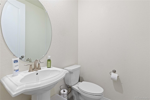 bathroom featuring a textured wall, a sink, and toilet