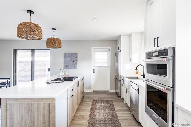 kitchen with a center island, hanging light fixtures, light hardwood / wood-style flooring, white cabinets, and appliances with stainless steel finishes