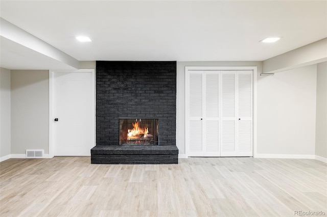 unfurnished living room with a brick fireplace and light wood-type flooring