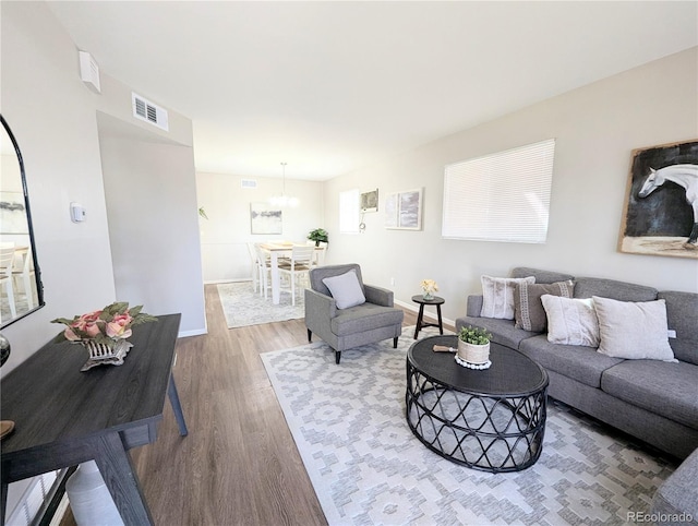 living area with wood finished floors, visible vents, a chandelier, and baseboards