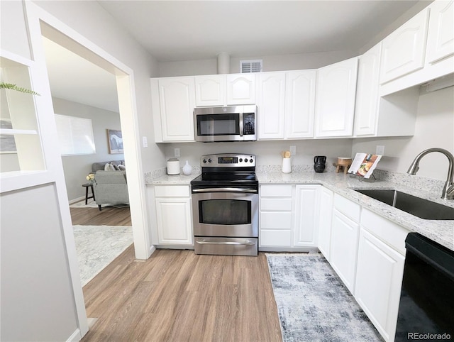 kitchen featuring a sink, light stone countertops, light wood finished floors, and stainless steel appliances