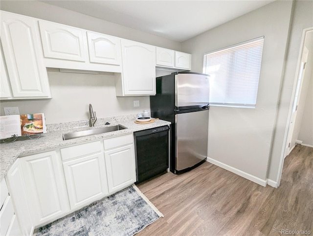 kitchen with light wood finished floors, freestanding refrigerator, black dishwasher, and a sink