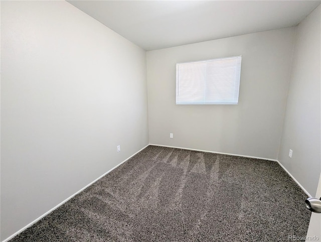 spare room featuring dark colored carpet and baseboards