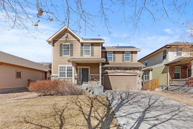 traditional-style house featuring a garage, stone siding, driveway, and roof mounted solar panels