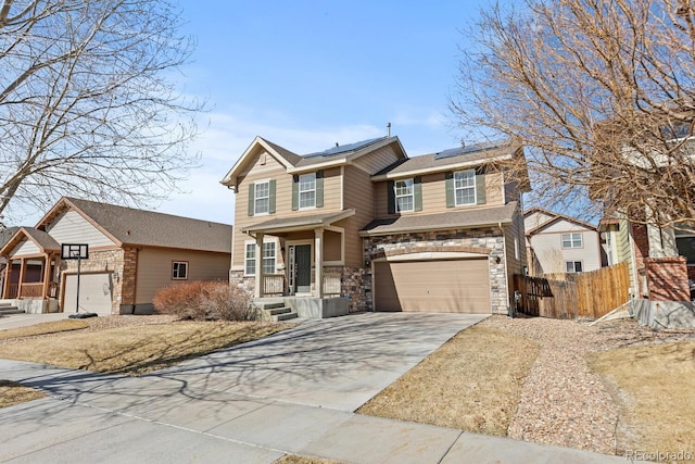 view of front of property with roof mounted solar panels, fence, a garage, stone siding, and driveway