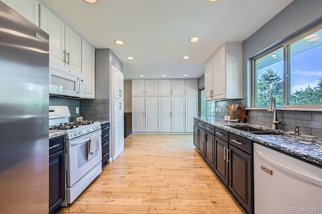 kitchen with white appliances, a sink, light wood-style floors, white cabinets, and dark stone counters