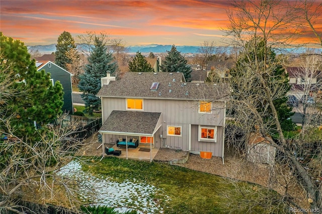 back house at dusk featuring a mountain view, a patio area, and a yard