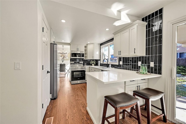 kitchen with hardwood / wood-style flooring, decorative backsplash, white cabinetry, and stainless steel appliances