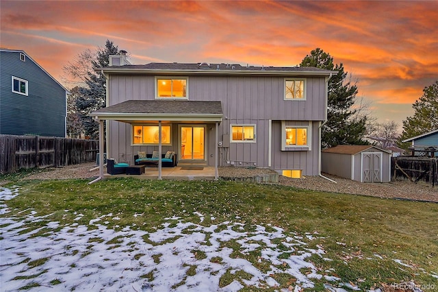 snow covered back of property with outdoor lounge area, a patio area, a storage shed, and a lawn