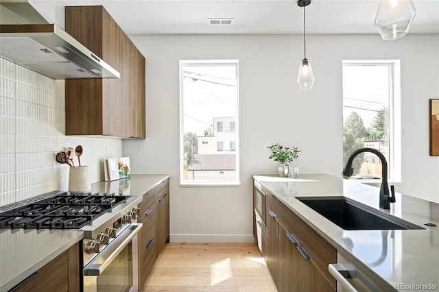 kitchen with stainless steel stove, sink, backsplash, hanging light fixtures, and wall chimney range hood