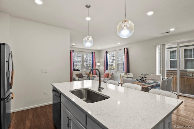 kitchen with appliances with stainless steel finishes, decorative light fixtures, sink, dark wood-type flooring, and a kitchen island with sink