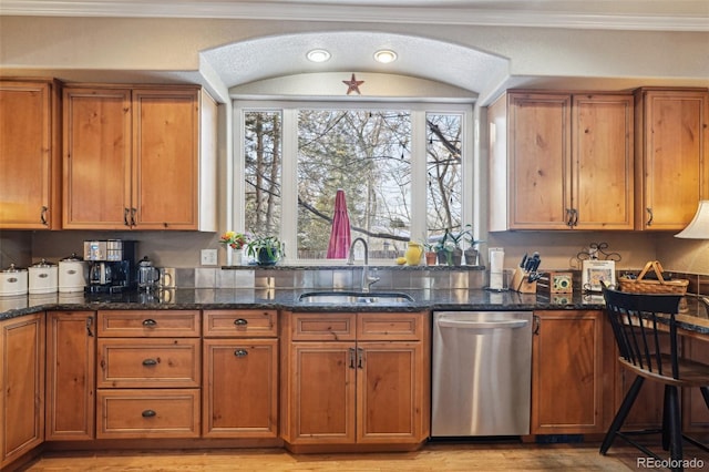 kitchen featuring a sink, stainless steel dishwasher, brown cabinetry, dark stone countertops, and crown molding