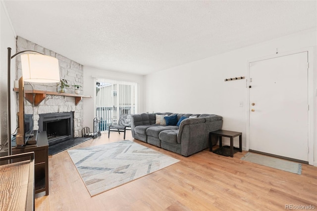 living room featuring a stone fireplace, a textured ceiling, and light hardwood / wood-style flooring