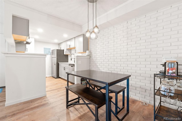 dining space featuring brick wall, sink, ornamental molding, a textured ceiling, and light hardwood / wood-style flooring