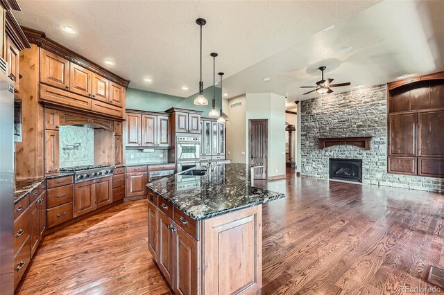 4725 Palmer Ridge Dr, Parker, CO 80134 - kitchen with a ceiling fan, light wood-style flooring, a center island with sink, pendant lighting, and dark stone counters