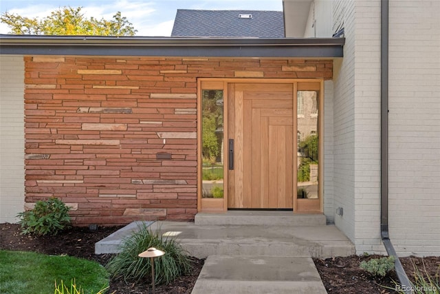 entrance to property with brick siding and a shingled roof