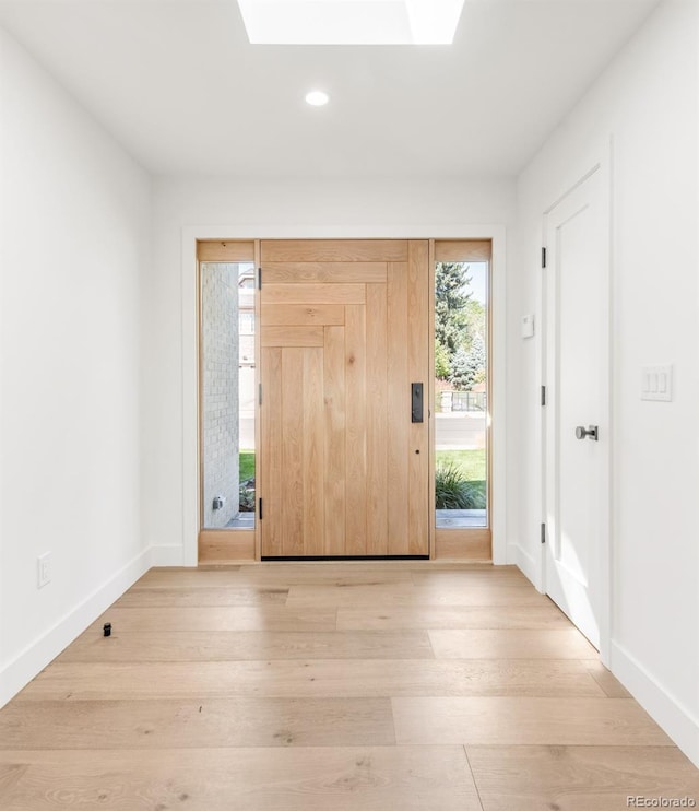 foyer entrance featuring a skylight, baseboards, light wood-style floors, and recessed lighting