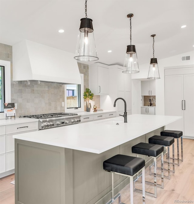 kitchen with visible vents, a large island, custom range hood, stove, and light countertops