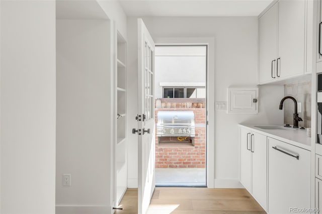 interior space with light countertops, light wood-type flooring, a sink, and white cabinets