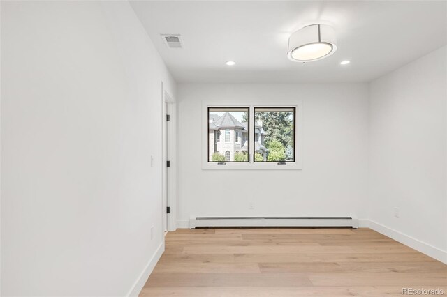 spare room featuring light wood-style floors, a baseboard radiator, visible vents, and baseboards