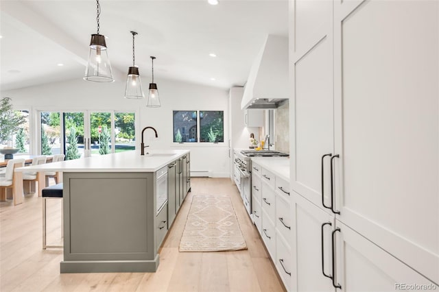 kitchen featuring light countertops, a large island with sink, high end stove, premium range hood, and a sink