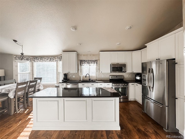 kitchen featuring a sink, stainless steel appliances, white cabinetry, dark countertops, and a center island