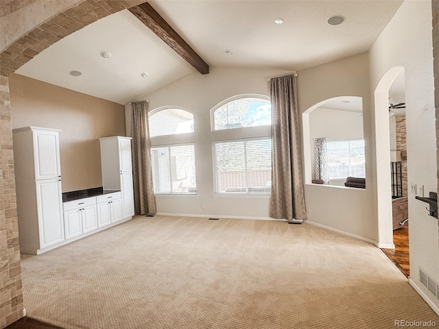 unfurnished living room featuring visible vents, arched walkways, baseboards, light colored carpet, and vaulted ceiling with beams