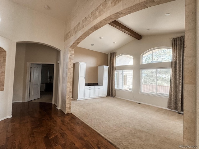 unfurnished living room featuring beam ceiling, arched walkways, wood finished floors, and high vaulted ceiling