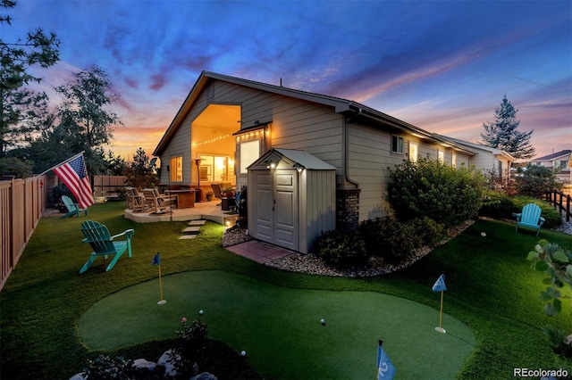 back of house at dusk featuring a patio area, a shed, an outdoor structure, and a fenced backyard