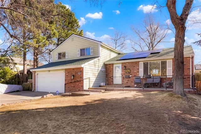 split level home with driveway, an attached garage, a shingled roof, brick siding, and solar panels