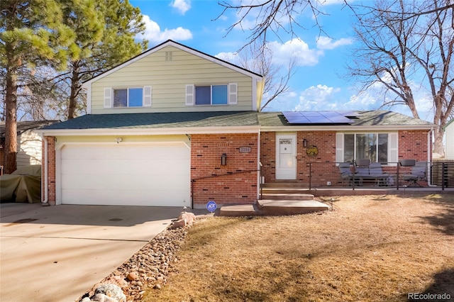 split level home featuring roof with shingles, solar panels, an attached garage, concrete driveway, and brick siding