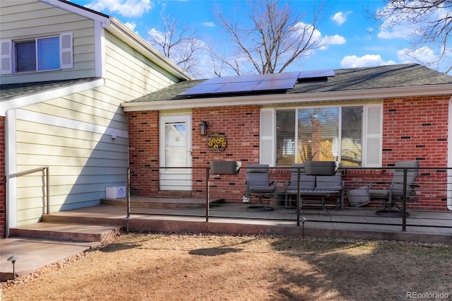 rear view of house featuring brick siding, roof mounted solar panels, and a shingled roof