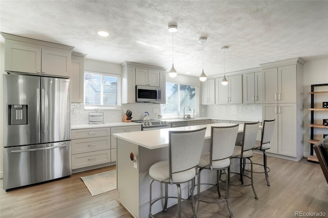 kitchen with a wealth of natural light, a breakfast bar area, light wood-type flooring, and appliances with stainless steel finishes