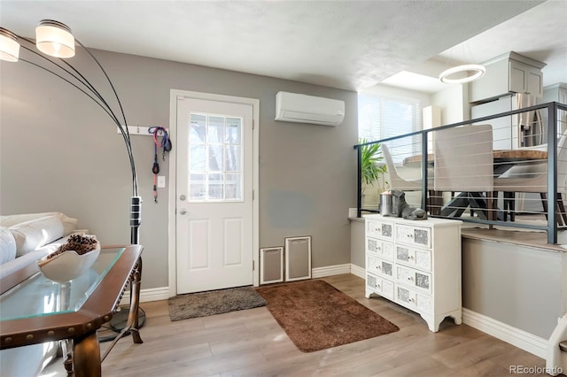 foyer with baseboards, light wood finished floors, and a wall mounted AC