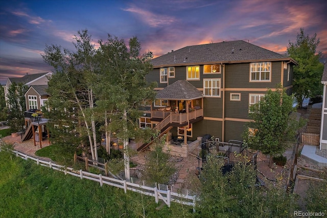 6927 Winter Ridge Pl, Castle Pines, CO 80108 - back of property at dusk with fence private yard, a patio, a wooden deck, roof with shingles, and stairs