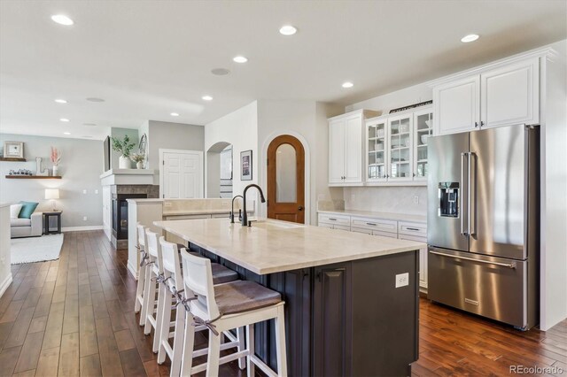 6927 Winter Ridge Pl, Castle Pines, CO 80108 - kitchen featuring high end fridge, a sink, arched walkways, a kitchen island with sink, and dark wood-style flooring