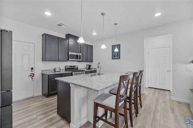 kitchen featuring sink, hanging light fixtures, light stone counters, a kitchen island with sink, and appliances with stainless steel finishes