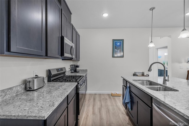 kitchen featuring pendant lighting, sink, light wood-type flooring, appliances with stainless steel finishes, and light stone counters