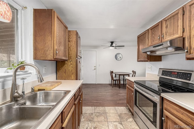 11886 Birch Dr, Thornton, CO 80233 - kitchen with stainless steel electric range, a sink, under cabinet range hood, brown cabinets, and a ceiling fan