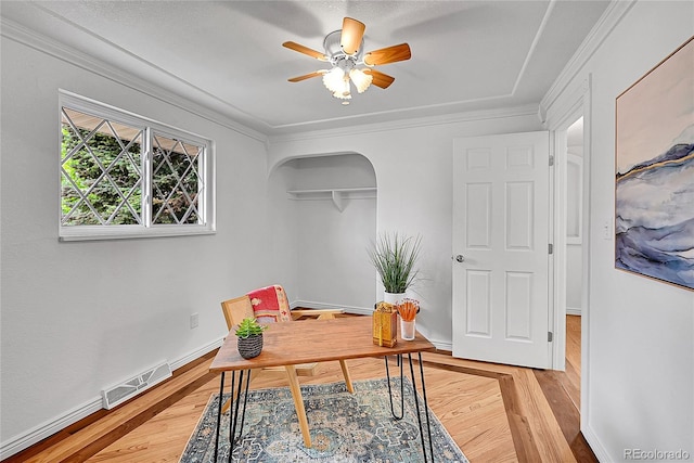 office featuring a ceiling fan, visible vents, baseboards, arched walkways, and light wood-style floors