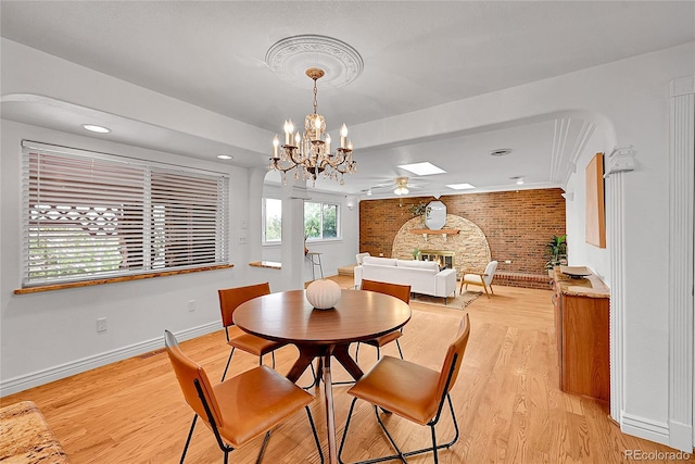 dining space featuring baseboards, light wood finished floors, an inviting chandelier, brick wall, and a skylight