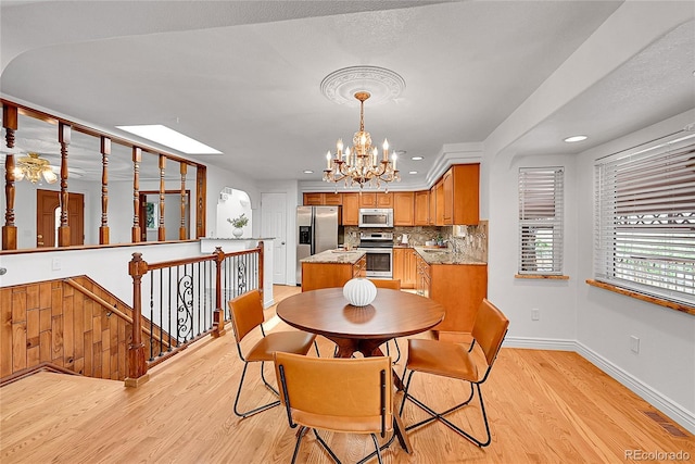dining room with a skylight, recessed lighting, an inviting chandelier, baseboards, and light wood-style floors
