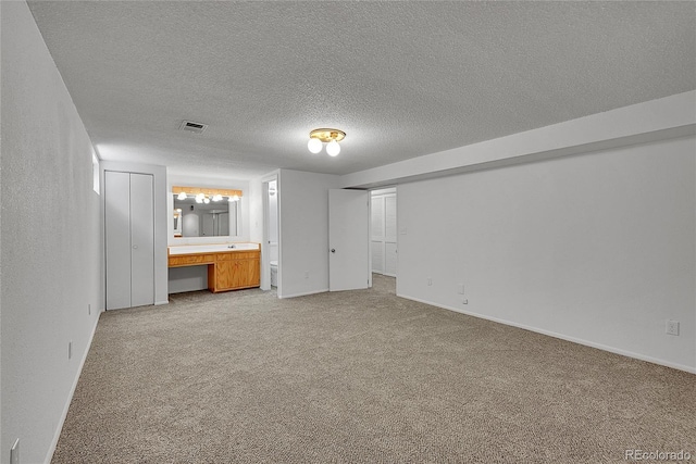 interior space with ensuite bathroom, a textured ceiling, visible vents, carpet floors, and baseboards