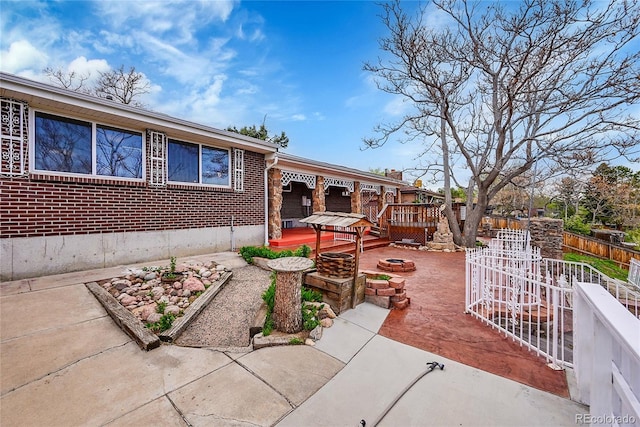 view of front of house featuring a patio area, fence, brick siding, a wooden deck, and an outdoor fire pit