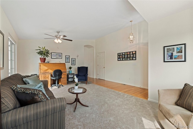 carpeted living area featuring baseboards, arched walkways, ceiling fan, and wood finished floors