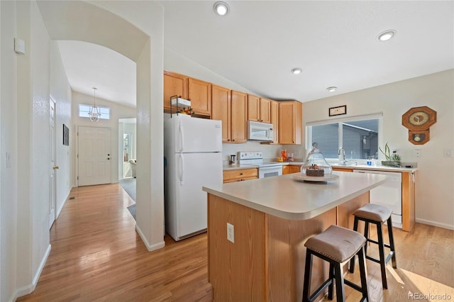 kitchen with white appliances, vaulted ceiling, light countertops, light wood-type flooring, and a center island