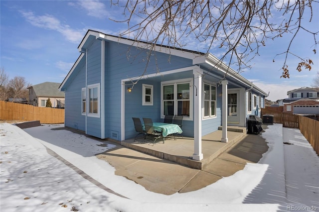 snow covered house with fence private yard and a patio area