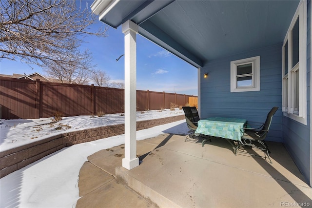 snow covered patio with a fenced backyard