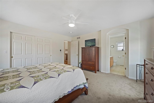 bedroom featuring arched walkways, light carpet, visible vents, a closet, and ensuite bath