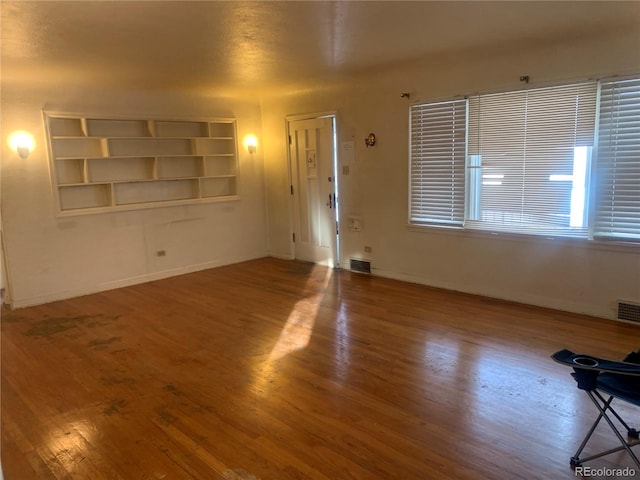 unfurnished living room featuring wood-type flooring and built in features